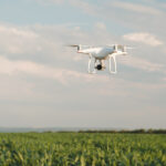 White drone hovering in a bright blue sky. Drone copter flying with digital camera